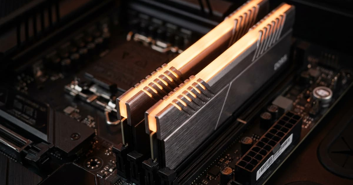 Two DDR RAM modules with orange-lit heat spreaders installed in a motherboard, illustrating memory speed and RAM latency